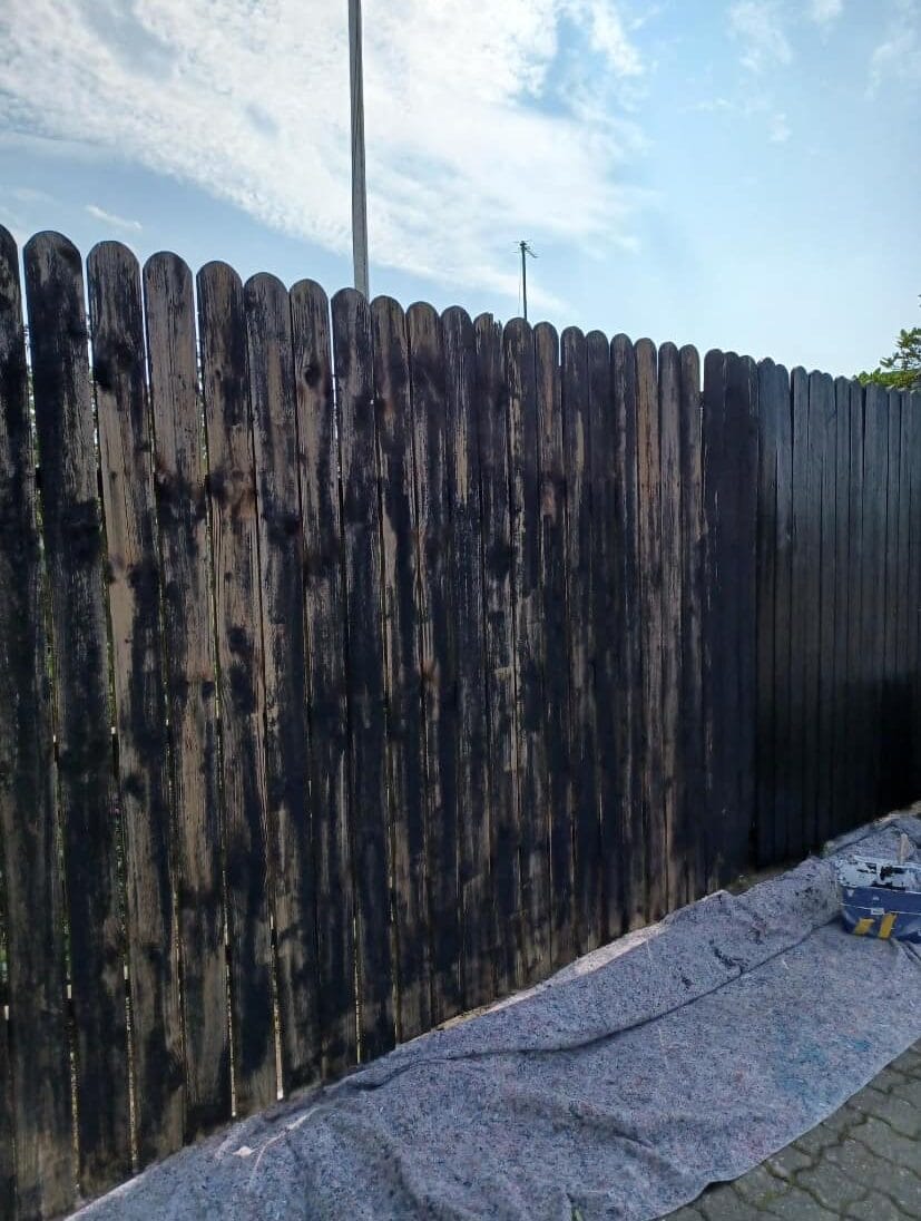 Træhegn bliver malet sort udendørs