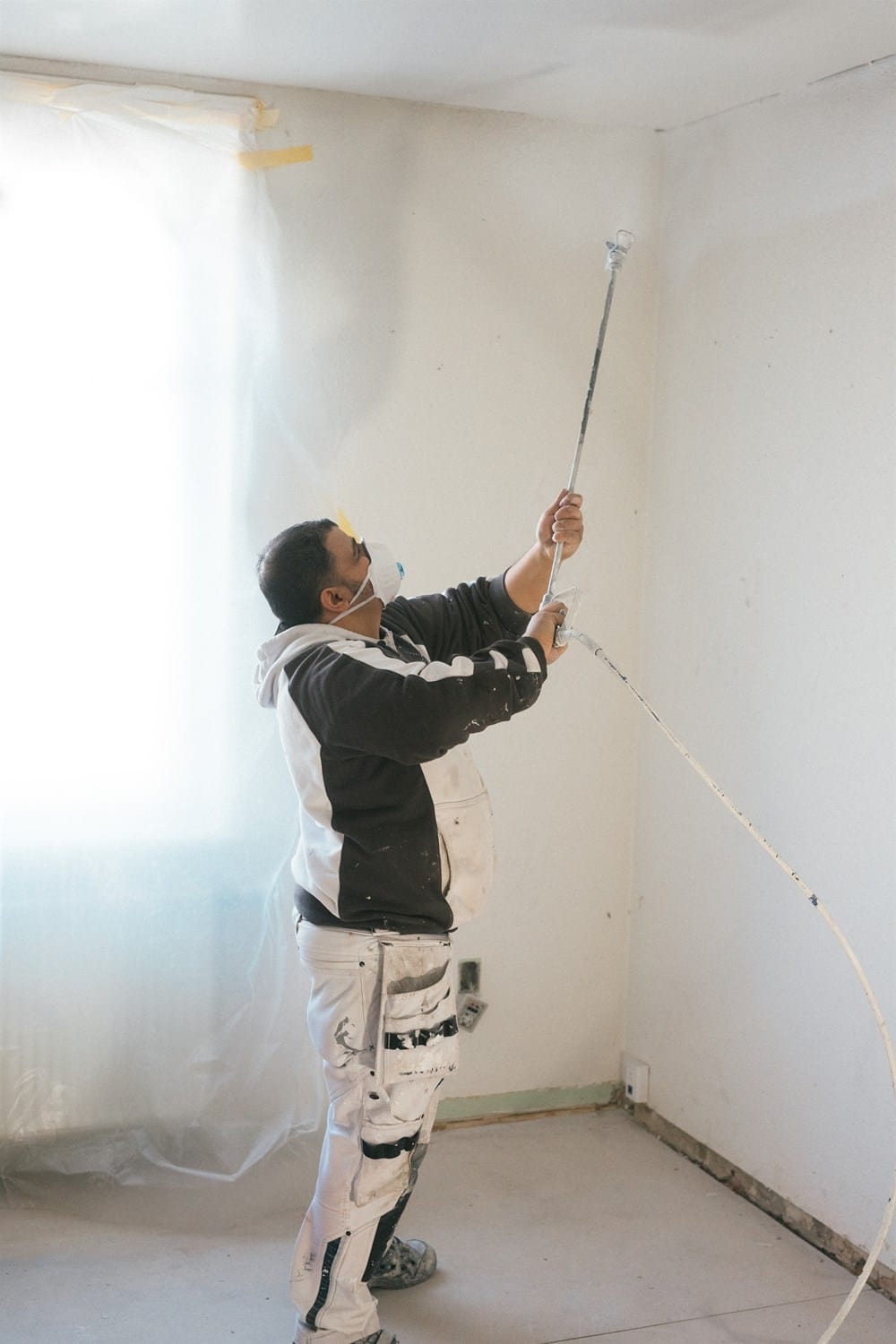 Maler sprøjter maling på loft i rum